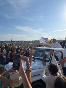 Pope Leo waiving happily to the large crowd of pilgrims while inside the popemobile. 