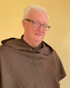 Headshot photo of Fr Miceal O'Neill, O.Carm wearing brown habit on gold background. 